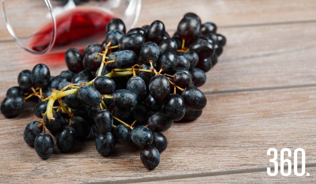 Uvas en primer plano y, al fondo, una copa de vino tinto evocan el origen y la tradición de esta bebida milenaria.