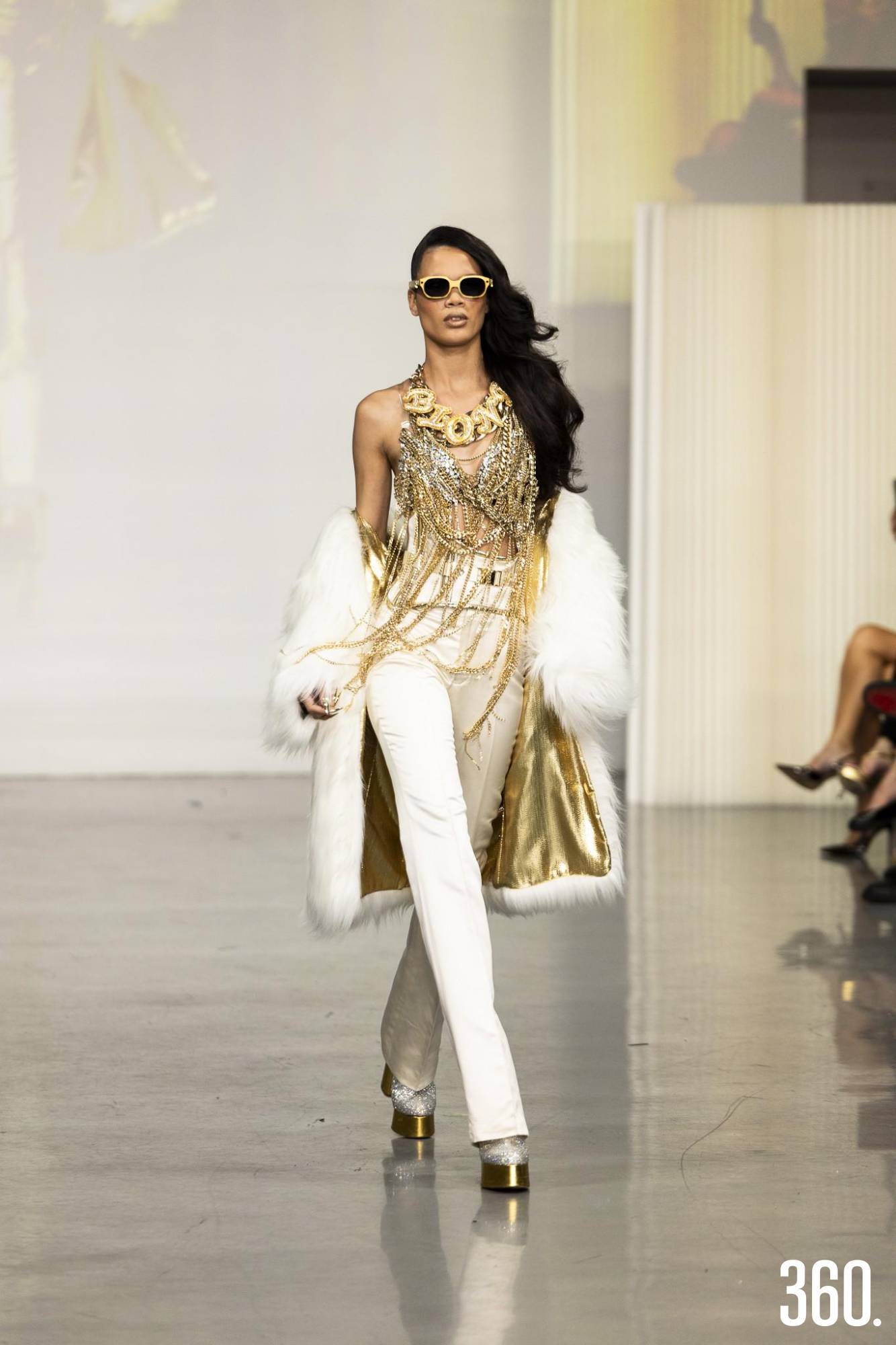 $!Traje blanco de pantalón recto combinado con un top dorado de collares y un abrigo de textura suave.