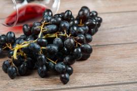 Uvas en primer plano y, al fondo, una copa de vino tinto evocan el origen y la tradición de esta bebida milenaria.