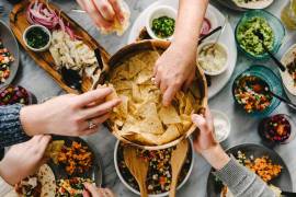 Manos compartiendo comida al estilo de un antiguo simposio: disfrutar primero, cuestionar después.