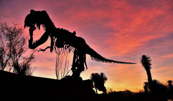 La silueta de un dinosaurio se recorta contra el cielo mientras el sol cae sobre Saltillo.
