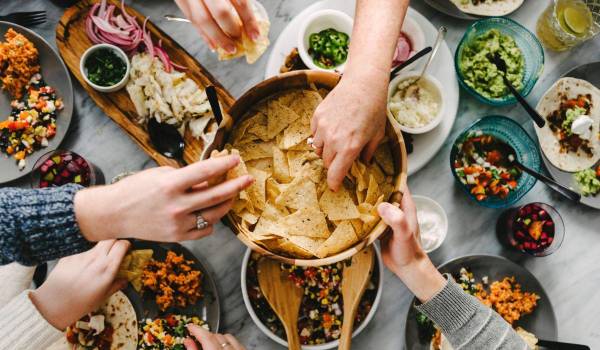 Manos compartiendo comida al estilo de un antiguo simposio: disfrutar primero, cuestionar después.